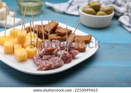 Toothpick appetizers. Pieces of sausage, cheese and croutons on light blue wooden table, closeup. Space for text Royalty-Free Stock Photo #2250049663