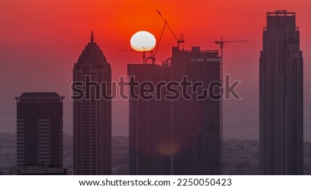 Skyline with modern architecture of Dubai business bay towers at sunset  with big red sun. Aerial close up view with canal and construction site