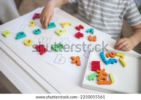Childish hands holding alphabet wooden board with colored font letters in cells closeup. Boy girl kid arms intellect game playing early development primary education letters learning Royalty-Free Stock Photo #2250055561