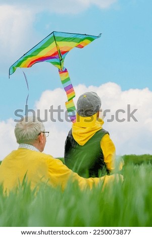 Focus on the rainbow kite flying, an elderly man and a grandson are looking at the sky, turned back. Family active outdoors game and playtime positive. High quality photo Royalty-Free Stock Photo #2250073877