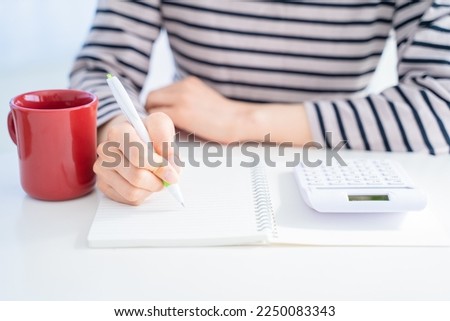 A woman keeping a household account book in a bright living room. Royalty-Free Stock Photo #2250083343