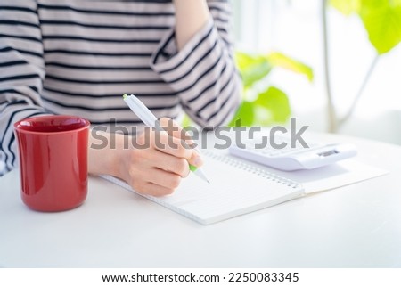 A woman keeping a household account book in a bright living room. Royalty-Free Stock Photo #2250083345