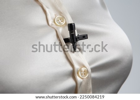 small microphone on a clothespin for voice recording is attached to a woman shirt on the chest
