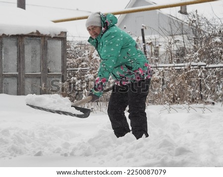 An elderly woman cleans snow in the yard on a winter snowy day.Healthy lifestyle.Winter fun.Blurred image and flying snow.