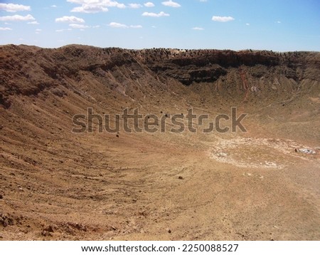 A large meteor crater with brown rocks scattered and a white ring in the center of the impact at Meteor Crater near Winslow Arizona