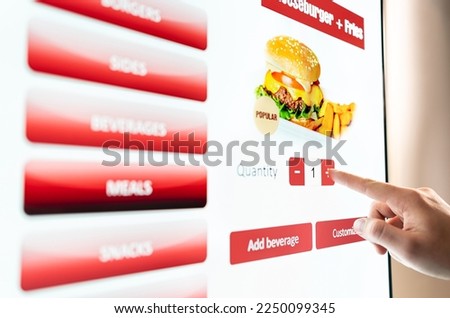 Self service order kiosk and digital menu in fast food burger restaurant. Touch screen in vending machine. Man using electronic selfservice technology and buying meal and paying. Royalty-Free Stock Photo #2250099345