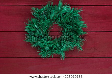 Green Christmas wreath hanging on dark red rustic wooden background