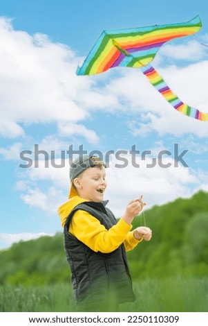 Focus on the child's hands launching a rainbow kite in the sky and looking at the camera. Active outdoors game and playtime positive. High quality photo Royalty-Free Stock Photo #2250110309