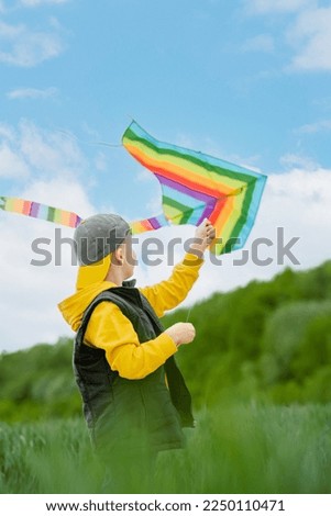 Focus on the child's hands launching a rainbow kite in the sky. Active outdoors game and playtime positive. High quality photo Royalty-Free Stock Photo #2250110471