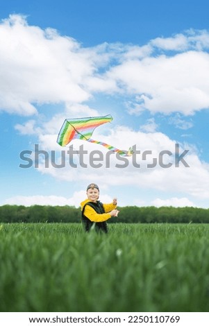 Focus on the child's hands holding a rainbow kite in the middle of a green field and looking at the camera. Active outdoors game and playtime positive. High quality photo Royalty-Free Stock Photo #2250110769