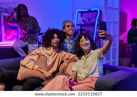 Happy youthful intercultural friends in casualwear taking selfie at home party while relaxing on comfortable couch in living room Royalty-Free Stock Photo #2250110837