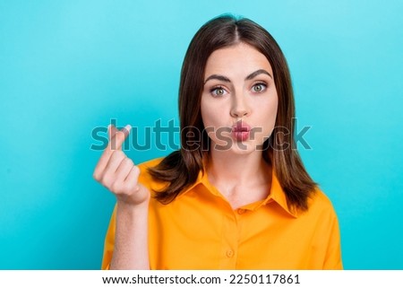 Photo of charming funny lady wear orange shirt sending you kiss showing korean love sign isolated turquoise color background