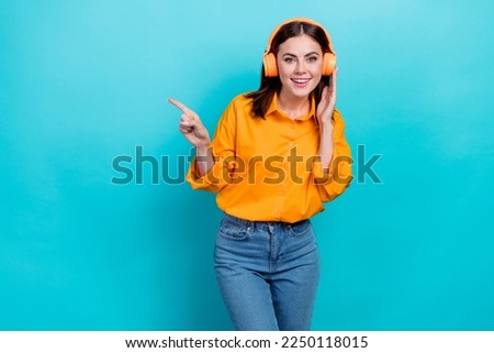 Photo of pretty cute lady wear orange shirt listening songs pointing empty space isolated turquoise color background