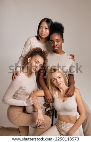 Multiracial women in beige basic outfit hugging and posing on camera, isolated in studio. Portrait of young ladies looking at camera, friendly and pleasant, looking calm, pretty. beige background Royalty-Free Stock Photo #2250118573