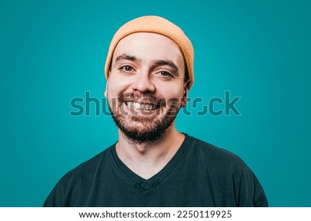 A male figure dressed in a yellow cap, in a studio shot with a blue background, is laughing heartily, his face alight with happiness and positivity, while looking into the camera with ample copy space Royalty-Free Stock Photo #2250119925
