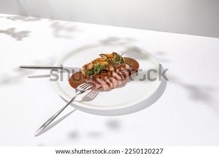 Roasted duck breast with potato gratin and sauce on light background. Fried duck fillet on white plate with hard shadows. Elegant summer menu. French cuisine - duck breast with gravy