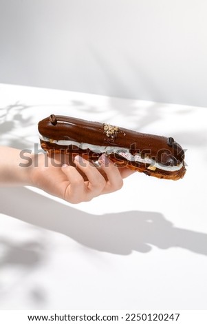 Female hand holding chocolate eclair. Woman take chocolate eclair. Hand with dessert. Trendy dessert menu. Coffee eclair with person Royalty-Free Stock Photo #2250120247