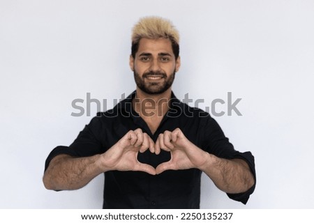 Close-up of heart gesture made by joyful businessman. Male Caucasian model with brown eyes, ombre painted hair and beard in black shirt showing heart sign with his hands. Love, feeling concept