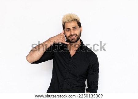 Winsome young man making phone gesture. Male Caucasian model with brown eyes, ombre painted hair and beard in black shirt smiling showing call me back sign. Coquetry, advertisement concept