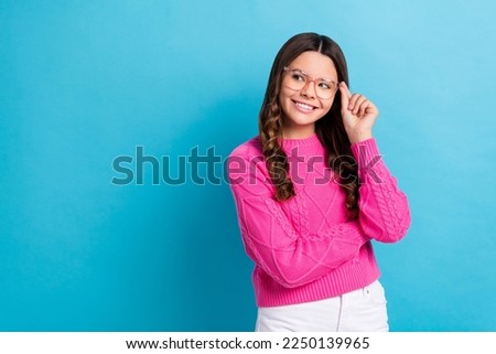 Photo of young curly brown hair schoolgirl teenager wear pink jumper touch glasses minded look empty space isolated on blue color background