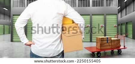 Man near storage room. Guy with boxes back camera. Man in corridors of storage company. Rental storage units. Human looks at closed warehouse containers. Trolley with boxes near businessman Royalty-Free Stock Photo #2250155405