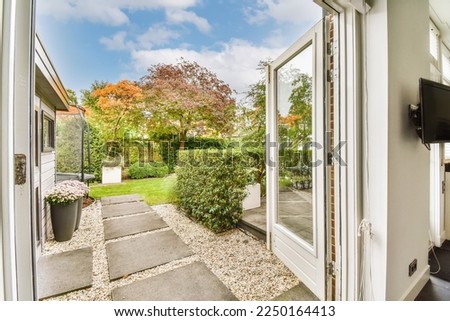 the outside of a house from inside an open door looking out onto a garden with trees and bushes in the background