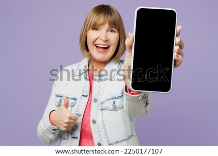 Elderly blonde woman 50s years old wears casual clothes denim jacket t-shirt hold use close up mobile cell phone blank screen workspace area show thumb up isolated on plain pastel purple background Royalty-Free Stock Photo #2250177107