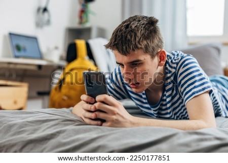 Teenage boy is surfing on the internet using his phone Royalty-Free Stock Photo #2250177851