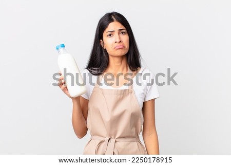 pretty hispanic chef woman feeling sad and whiney with an unhappy look and crying and holding a milk bottle