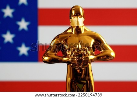 Hollywood Golden Oscar Academy award statue in mask on American flag background. Success and victory concept.