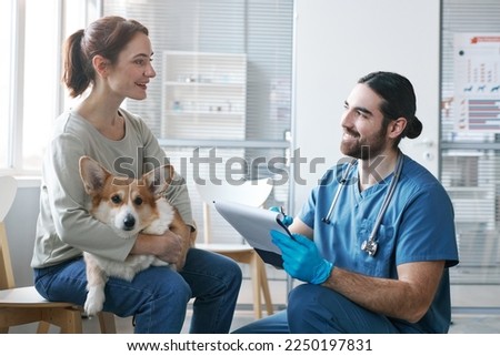 Young male veterinarian with medical document talking to owner of purebred welsh pembroke corgi dog during consultation Royalty-Free Stock Photo #2250197831