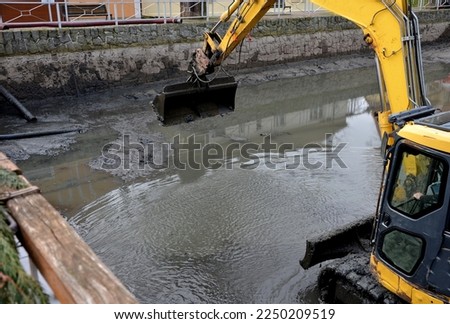 removing sedimentary sludge from the bottom of a pond or a swimming lake in the village. the muddy water cleaning set with pumps vacuums the sump. a crawler excavator cleans bottom from deposits soil  Royalty-Free Stock Photo #2250209519