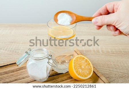 Close up of woman hand pouring baking soda in drinking glass with water and lemon juice, health benefits for digestive system concept.  Royalty-Free Stock Photo #2250212861