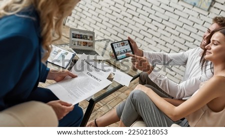 Young caucasian couple show choosed place for rest on digital tablet to female tourist agent with travel insurance and contract in travel agency office. Client service. Vacation, tourism and journey Royalty-Free Stock Photo #2250218053