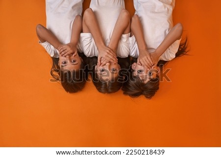 Partial top view of caucasian girls cover mouth and look at camera. Girlfriends of zoomer generation. Modern youngster lifestyle. Friendship. Speak no evil. Orange background. Studio shoot. Copy space