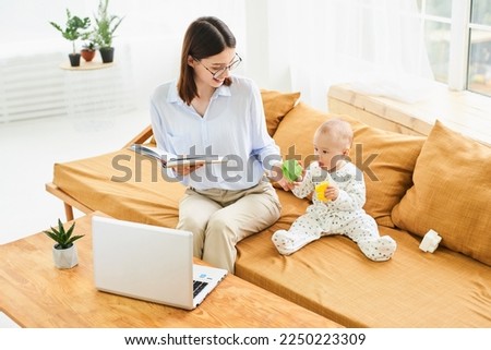 Young single mother mom with toddler newborn baby infant son using laptop, searching web, watching cartoons together. Working from home on maternity leave, freelancer, looking for kids goods.