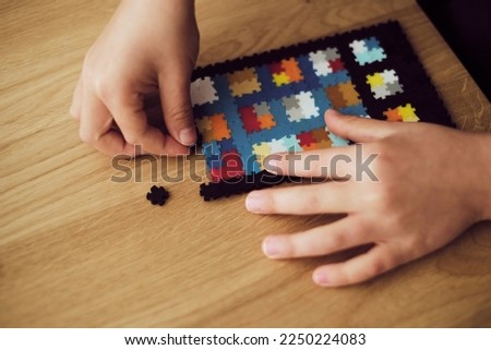 Child making the tablet made of plastic puzzle tiles over the wooden table. Children's creative game at home	