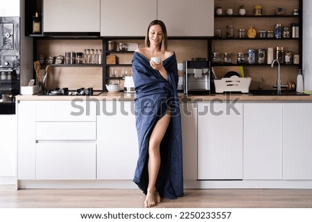 Sleepy positive woman wrapped in blue bed sheet drinking coffee in the morning in the kitchen Royalty-Free Stock Photo #2250233557