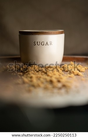 Picture of Sugar jar surrounded by granulated brown sugar on a wood surface