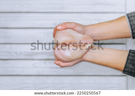 The girl holds pieces of raw, fresh chicken meat in the form of a heart on a wooden background. Photography, concept, lifestyle, copy space.