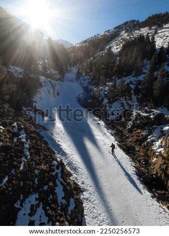 a backcountry skier climbs up a mountain pass on his way to the summit, projecting a long shadow behind him, the sun rises behind the mountains, vertical