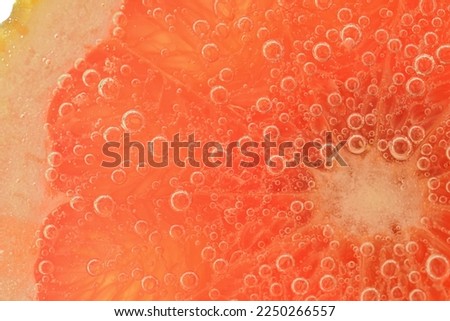 Slice of grapefruit in sparkling water. Grapefruit slice covered by bubbles in carbonated water. Grapefruit slice in water with bubbles. Macro shot of red grapefruit in bubble water. Tropical fruit.