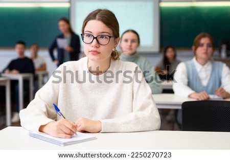 Concentrated teenage girl writing and studying at desk in classroom Royalty-Free Stock Photo #2250270723