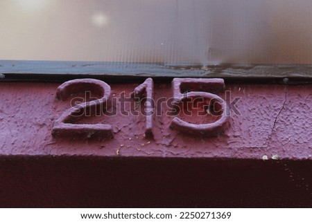 Number 215 on house wall with pink background. Two hundred and fifteen name of residence number.