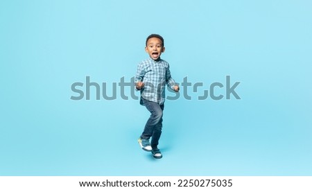 Yes. Happy little black kid boy shaking fists, making winner gesture, celebrating victory and win, standing over blue studio background wall, panorama Royalty-Free Stock Photo #2250275035