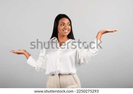 Glad confident millennial black female spreads her arms to sides, hold copy space, choice ad and offer, isolated on gray background, studio. Comparison of business, work, investment, study and startup Royalty-Free Stock Photo #2250275293