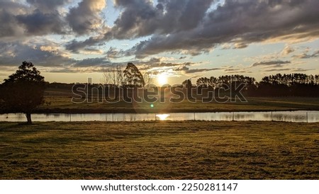 A picturesque farmstead sits at the edge of a lake, bathed in the warm light of a setting sun. Royalty-Free Stock Photo #2250281147