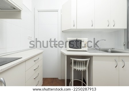 Corner of a humble conventional kitchen with white cabinets and countertops of the same color Royalty-Free Stock Photo #2250287913