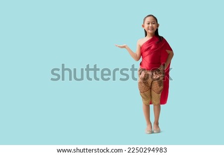 Full body Asian little girl in Thai national costumes with hand holding open palm up blank workspace, isolated on pastel plain light blue background