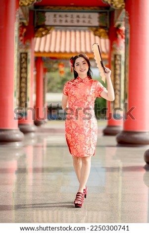 Vertical picture. Happy Chinese new year. A Asian woman wearing traditional cheongsam qipao dress holding fan and smile while visiting the Chinese Buddhist temple. Chinese new year concept